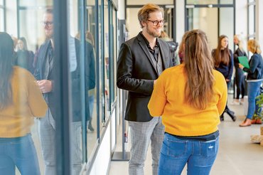 Ein Dozent und eine Studentin stehen im Flur und reden miteinander.