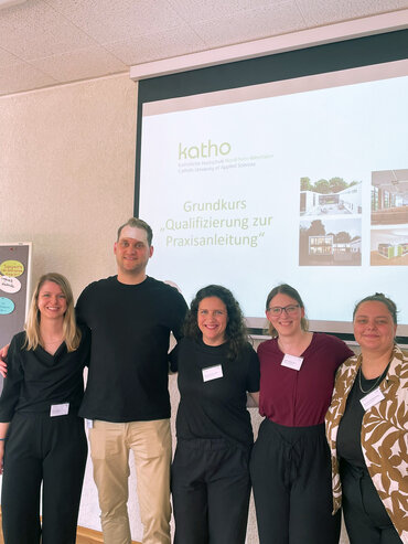 Ein Gruppenfoto des Praxisreferats, alle stehen nebeneinander, im Hintergrund ist die Präsentation der Folien auf der Wand zu sehen.t 