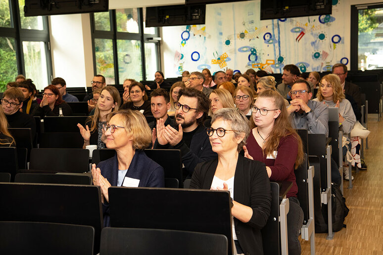 Teuilnhemende sitzen im Audimax und applaudieren. In der ersten Reihe sitzt u.a. die Rektorin der katho.s
