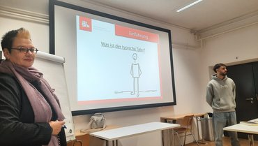 Zwei Personen stehen vor der Leinwand und referieren