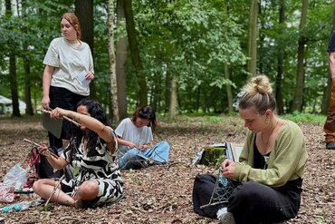 Personen sitzen auf dem Waldboden und schreiben.
