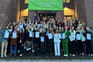 Eine Gruppe von Studierenden ist zu sehen, die glücklich Blumen in die Höhe halten.