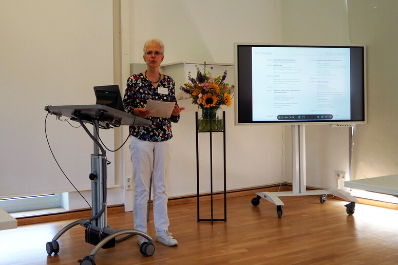Die Prorektorin steht im Seminarraum und spricht. Links von ihr steht ein Redepult, rechts ein Blumenstrauß und eine digitale Tafel.