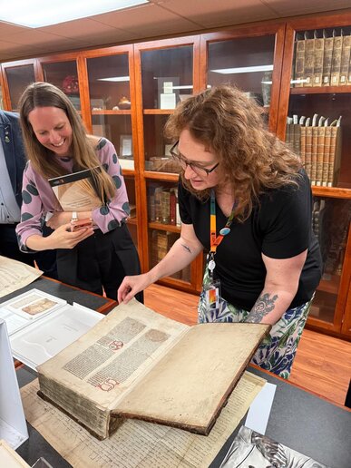 Lisa Jungkamp (Leiterin International Office) blättert mit einer Bibliotheksmitarbeiterin durch ein seltenes Buch der Saint Paul University.