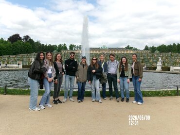 Die Studierenden stehen vor einem Brunnen im Schlosspark