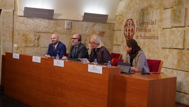 Rednerpanel in der Universidad Pontificia de Salamanca, bestehend aus mehreren Personen mit Tischschildern vor einer Steinmauer.