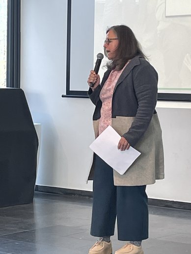 Silvia Hamacher steht auf der Bühne und begrüßt das Publikum