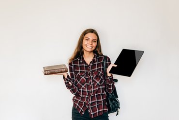 Eine Studentin hält in der einen Hand ein Tablet, in der anderen ein in Leder gebundenes Buch