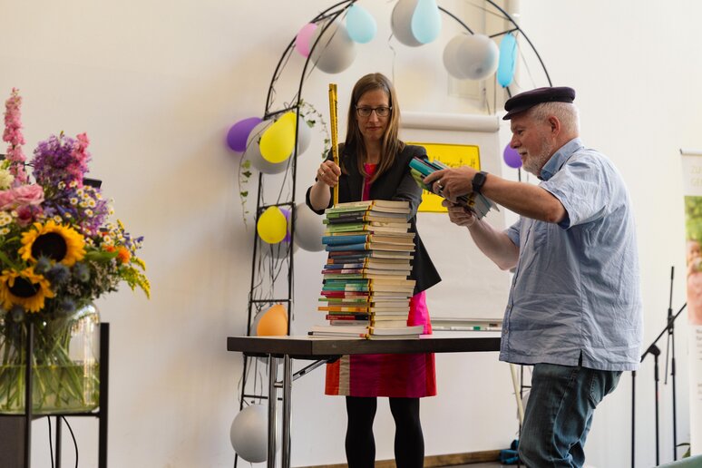 Der geehrte Kollege stapelt die von ihm veröffentlichten Bücher; der Stapel wird mit einem Zollstock gemessen.