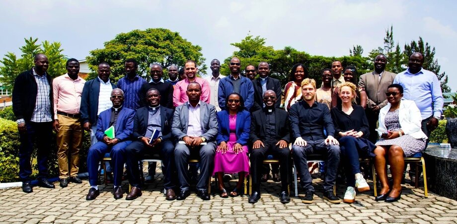 25 Personen auf einem Gruppenbild draußen vor grünen Bäumen. Die PErsonen stehen bzw. sitzen in zwei Reihen. In der ersten Reihe sitzen unter anderem Angela Wernberger und Felix Nuss.