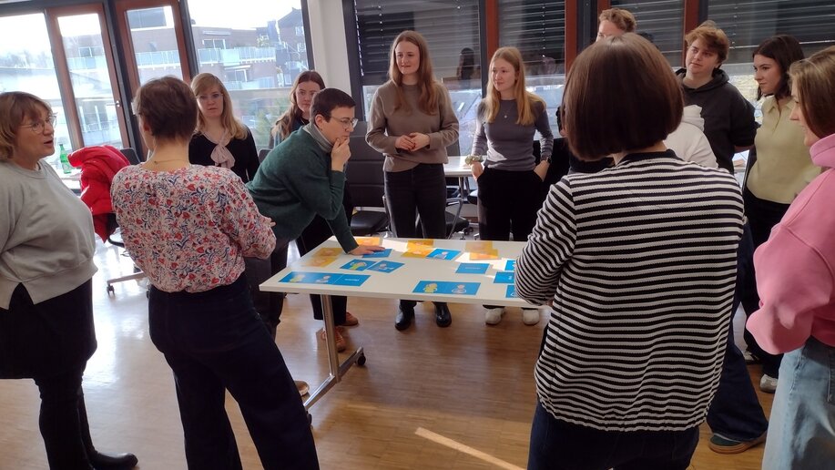 Schulungsteilnehmende stehen um einen Tisch mit blauen Karten, auf denen Begriffe wie neugierig oder ängstlich stehen.