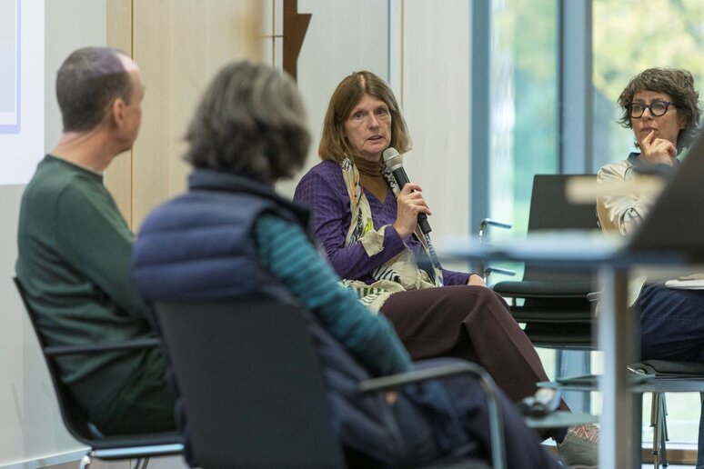 Vier Menschen sitzen zusammen. Eine Frau im lila Pullover hält das Mikrofon. Die anderen Personen schauen zu ihr.