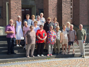 20 ältere Personen stehen für ein Gruppenfoto vor dem Eingang der katho in Paderborn. 