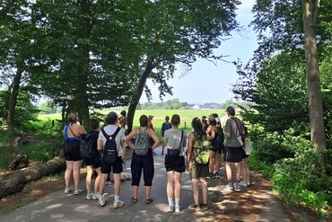 Die Seminarteilnehmenden stehen im Kreis in einem Waldstück. 