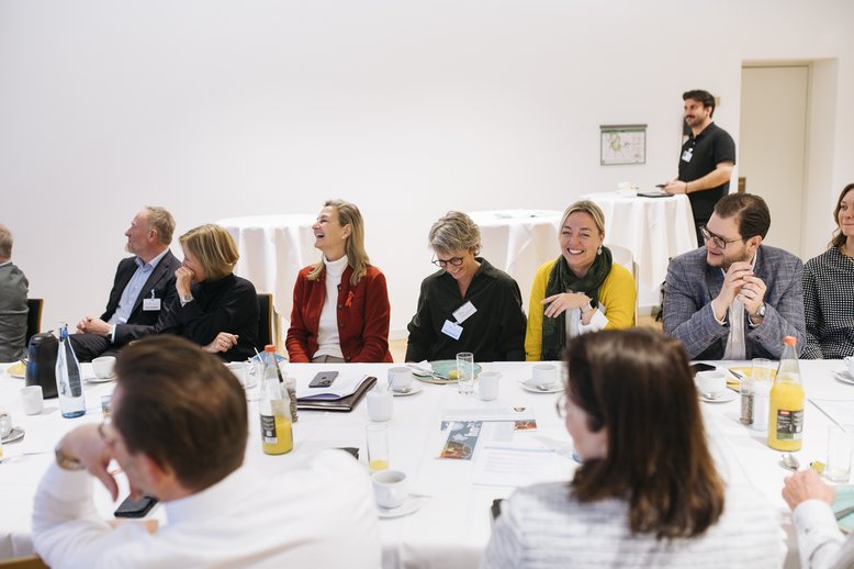 Teilnehmende sitzen an einem Tisch und lachen.