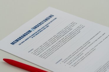 Auf einem Tisch liegt ein Papier mit der Überschrift "Memorandum of Understanding: For cross-border collaboration among higher-education institutions in the Euregio Meuse-Rhin (EMR)". Daneben liegt ein roter Kugelschreiber.