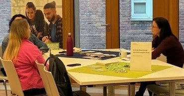 Eine Beratungssituation am Tag der offenen Tür ist zu sehen. Personen sitzen an einem Tisch und unterhalten sich. 