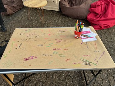 Ein Blatt Papier liegt auf einem Klapptisch, darauf sind handschriftliche Wünsche ans neuen Jahr notiert.