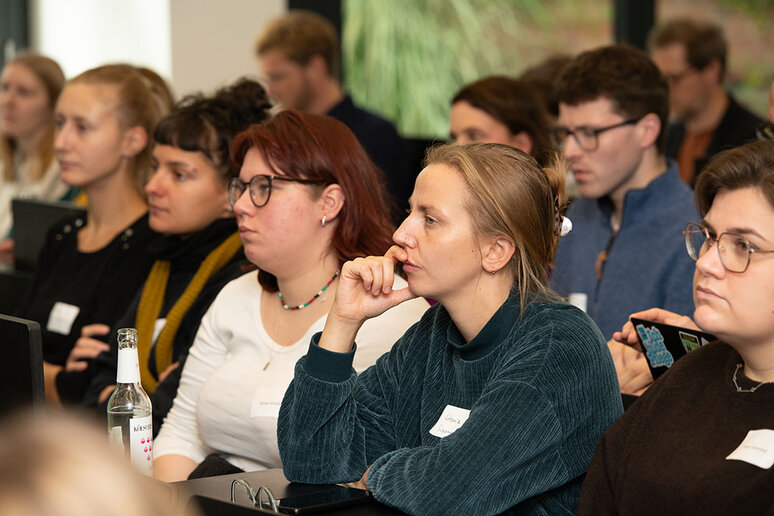 Teilnehmende in Sitzreihen hören zu.