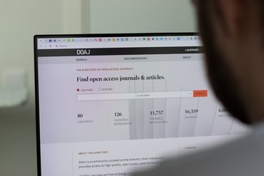 Ein Mann schaut auf einen Laptop, der die Website DOAJ mit der Überschrift Find open access journals and articles anzeigt.