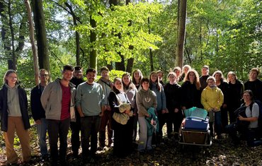 Die Teilnehmer_innen des Zertifikatskurses stehen als Gruppe im Wald zusammen.