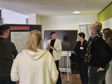 Die Teilnehmer_innen und die Referentin Prof.in Dr. Verlinden stehen im Kreis und diskutieren zum Thema "Arbeitsbelastung"