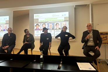 Fünf Personen sitzen bei einer Podiumsdiskussion auf Hockern.