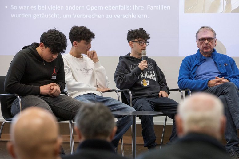 Drei Schüler sitzen nebeneinander, einer von den dreien spricht in ein Mikrofon.