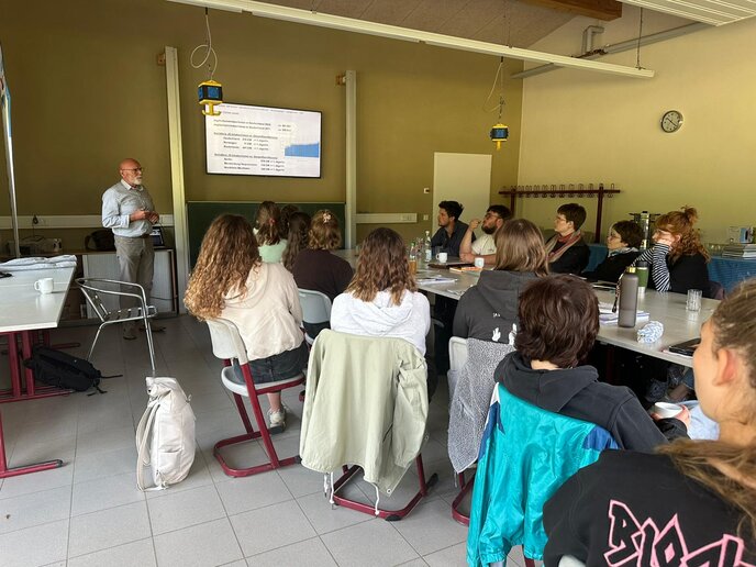 In einem Raum hören Teilnehmer_innen gespannt einem Referenten zu.