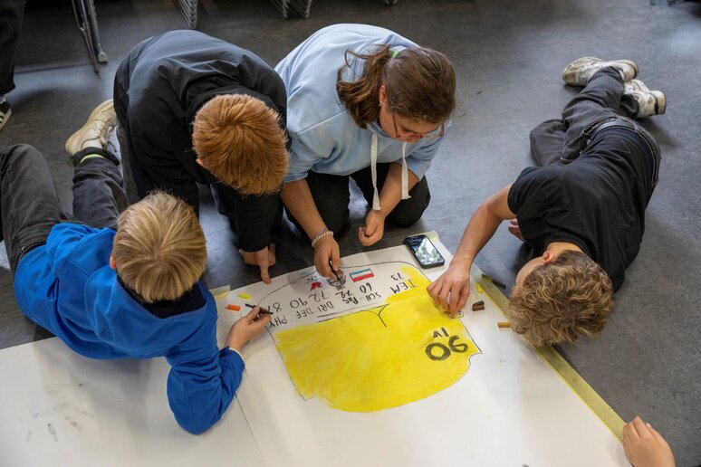 Schüler:innen sitzen auf dem Boden und malen mit Kohle.