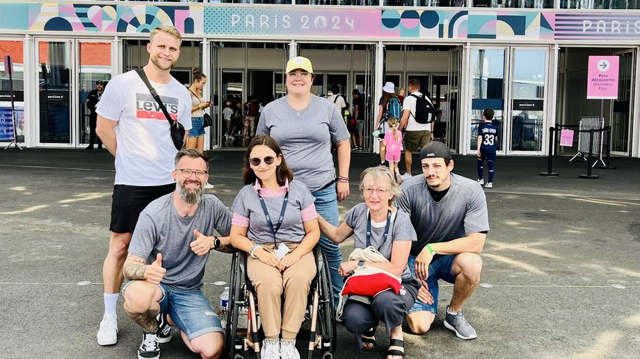 Das Foto zeigt in der vorderen Reihe einen Studenten hockend links neben den Professorinnen Sina Eghbalpour (im Rollstuhl) und Liane Schirra-Weirich (ebenfalls hockend). rechts hinter Schirra-Weirich hockt ein weiterer Student. HInter Eghpalbour steht eine Studentin und links neben ihr ein weiterer Student. Alle lächeln fröhlich in die Kamera.