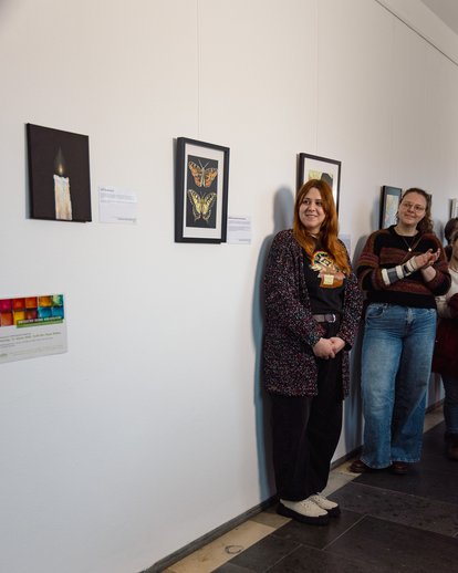 Studierende stellt ihre Bilder vor: Bild einer hellen Kerze auf dunklem Hintergrund (Ölmalerei) und bunte Schmetterlinge.