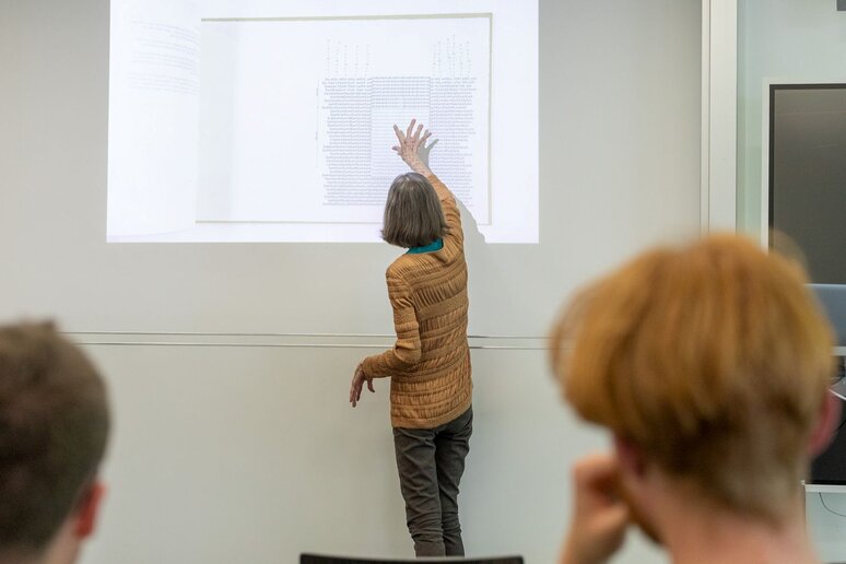 Diane Samuels steht vor der Grafik, die den Aufbau der Steine des Alphabetgartens zeigen.