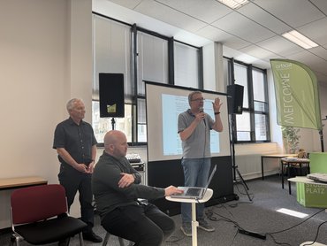 Marvin Hackfort sitzt am Laptop, die beiden Professoren stehen und sind im Gespräch mit dem Publikum.