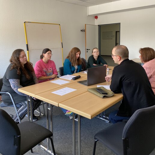 Inn einem Seminarraum sitzen Vertreterinnen von Lern- und Gedenkstätten sowie Absolvent_innen an einem Tisch und tauschen sich aus.