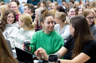 Studierende sitzend lächelnd und im Zwiegespräch in einem größeren Hörsaal.