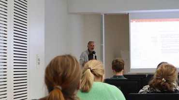 Professor mit Handmikrofon vor Zuschauerschaft