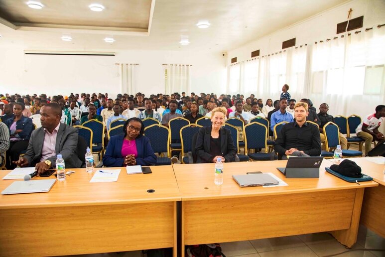 Im Vorlesungssaal sitzen zahlreiche Studierende. In der ersten Reihe an großen Tischen sitzen die Professor_innen der INES und der katho.