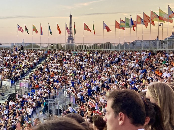 Aufnahme des vollbesetzten Stadions bei Dämmerung. Im Hintergrund wird das Bild von Nationalflaggen eingerahmt.