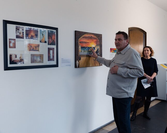 Ein Kollege vor seinen Bildern, im Hintergrund die Dekanin.