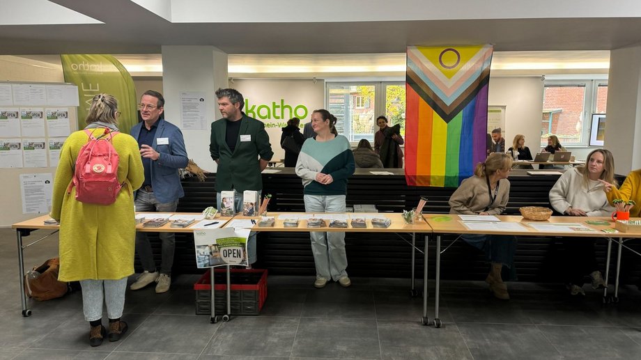 Eine Besucherin steht im Foyer der katho an einem Infostand mit Prof. Dr. Tiemann.
