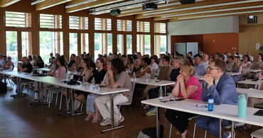 Viele Zuhörer_innen sitzen in Sitzreihen und verfolgen interessiert einen Vortrag im Audimax