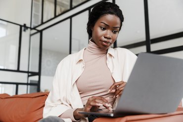 Eine Frau sitzt auf einem Sofa und schaut auf ihr Laptop.