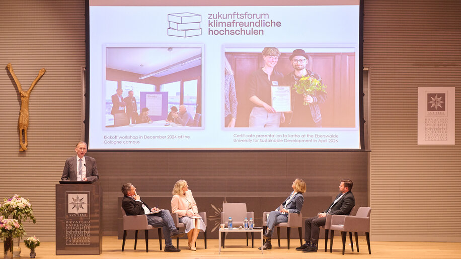 Vier Personen sitzen auf der Bühne, links am Stehpult spricht Kanzler Bernward Robrecht. Auf der Leinwand sind Fotos zu sehen mit der Überschrift "Zukunftsforum Klimafreundliche Hochschulen".