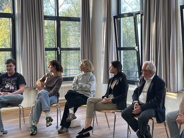 Das Bild zeigt Menschen, die im Stuhlkreis in einem Raum sitzen und miteinander reden.