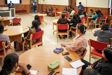 Indische Studierende sitzen zusammen an mehreren Tischen und hören dem Vortrag von Prof. Jox zu.