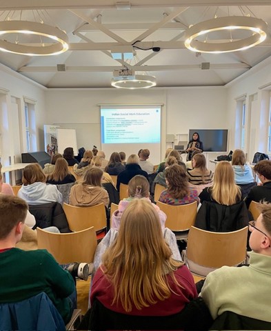 Es wird eine Lehrveranstaltung im Stil eines Seminars mit einer Rednerin am Pult gezeigt.