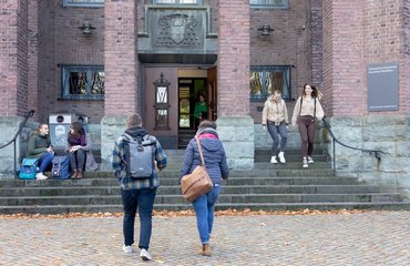 Vor dem Paderborner katho Gebäude gehen mehrere Studierende eine Treppe zum Haupteingang hoch.