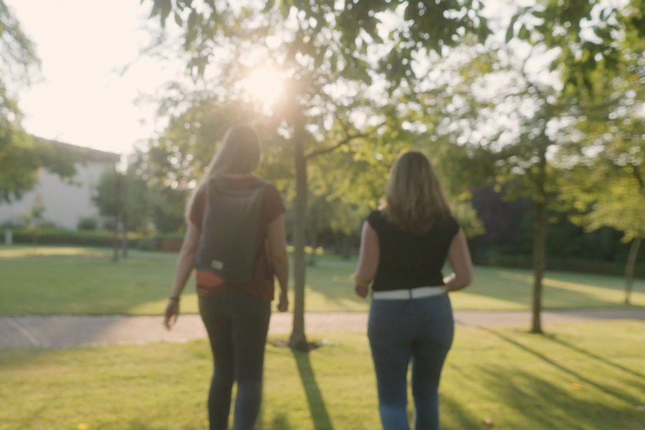 Zwei junge Studentinnen laufen im Sonnenlicht über die Wiese im Paderborner Park.