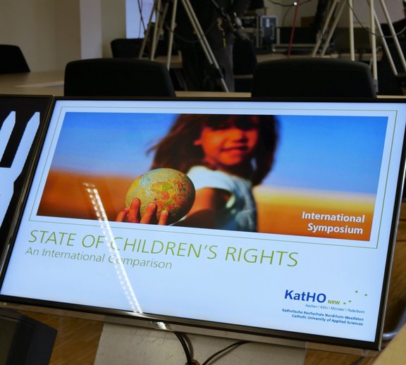 Während des Internationalen Online-Symposiums ist ein Bildschirm zu sehen, auf dem ein junges Mädchen einen Globus in der Hand hält. Unter dem Bild steht "State of children's rights - An International Comparison".